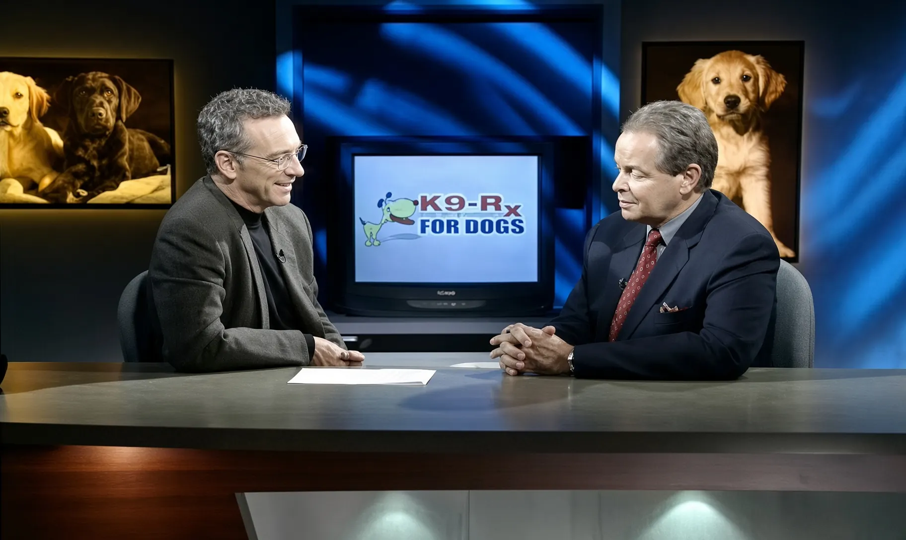 Still from the original K9-Rx television infomercial: two men at a studio desk with the K9-Rx For Dogs logo on a monitor behind them